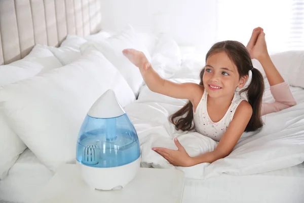 Cute little girl in bedroom with modern air humidifier