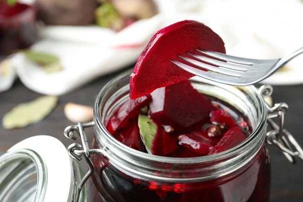 Fork with pickled beet over glass jar on wooden table, closeup — Stock Image Fork Pickled Beet Glass Jar Wooden Table Closeup Royalty Free Stock Photos