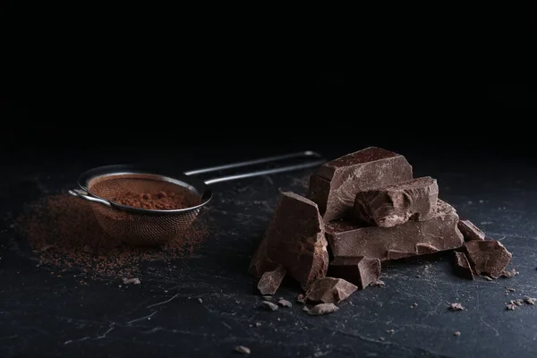 黑色桌子上的黑巧克力片和可可粉筛子 — 图库照片