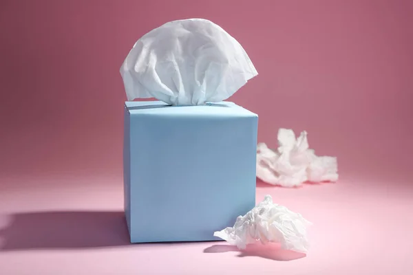 Box of paper tissues and used crumpled napkins on pink background