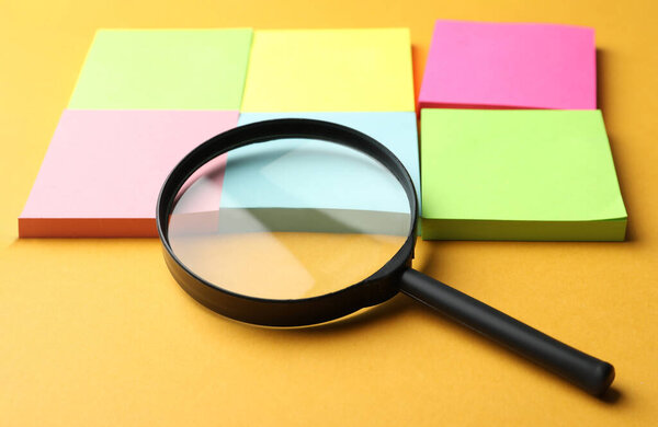 Увеличитель стекла и различные наклейки памяти на оранжевом фоне, крупным планом. Поиск концепции ключевых слов