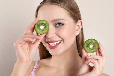 Bej arka planda kesilmiş kivi olan genç bir kadın. Vitamin zengini yiyecekler