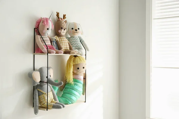 Shelf with cute toys on light wall indoors. Baby room interior element