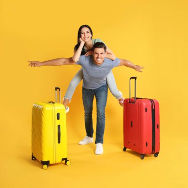 Sarı arka planda yaz gezisi için bavulları olan mutlu çift. Tatil gezisi