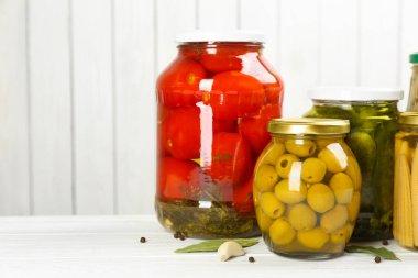 Beyaz ahşap arka planda farklı sebze turşusu olan cam kavanozlar. Metin için boşluk