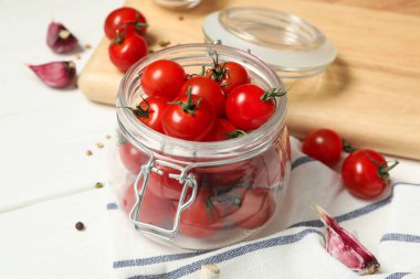 Taze kiraz domatesli turşu kavanozu ve beyaz ahşap masada baharatlar, yakın plan.