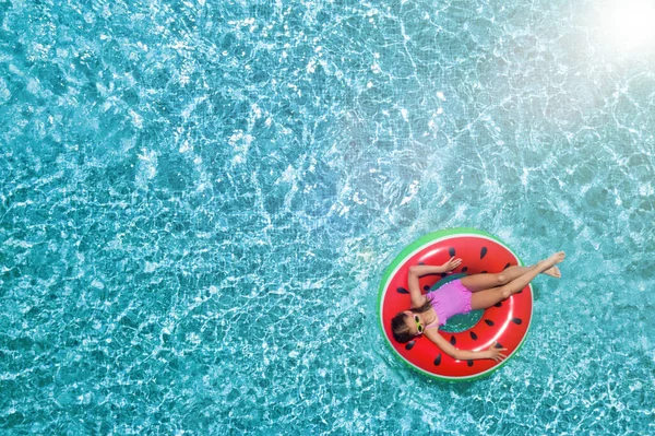 Cute little girl with inflatable ring in swimming pool, top view. Space for text