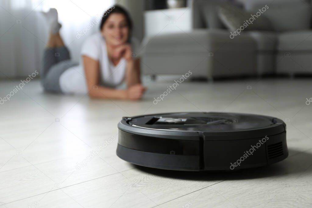Modern robotic vacuum cleaner and blurred woman on background