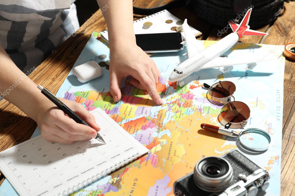 Woman marking calendar at table with world map, closeup. Travel during summer vacation