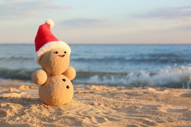 Kumsalda kumdan yapılmış, deniz kenarında Noel Baba şapkası olan bir kardan adam. Noel tatili