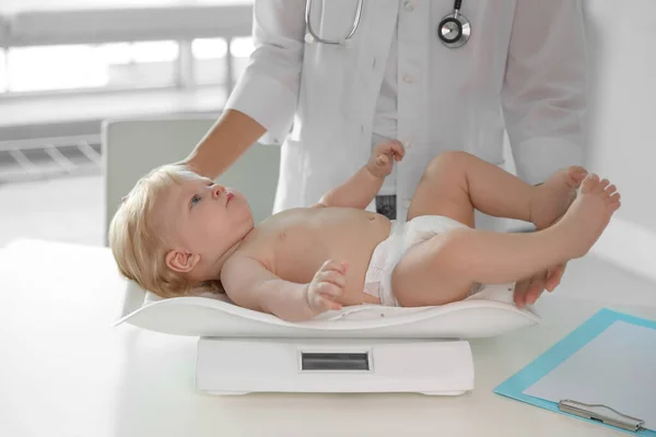 Pediatrician weighting baby on scale in hospital. Healthy growth