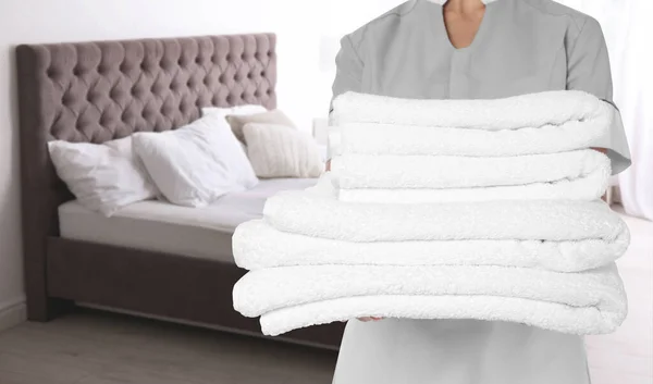 客室のベッドの近くにきれいな折り畳まれたタオルを持つ部屋のメイド クローズアップ — ストック写真
