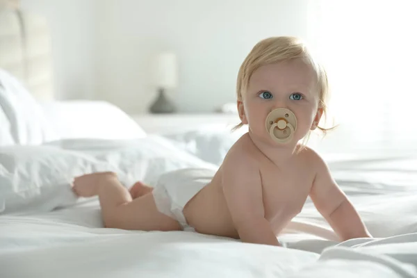 침대에 고무젖꼭지로 기저귀를 아기를 귀엽게 대한다 — 스톡 사진