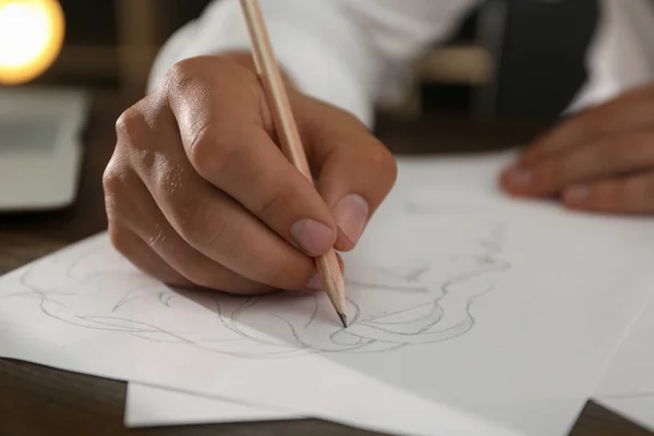 Man drawing portrait with pencil on sheet of paper at wooden table, closeup