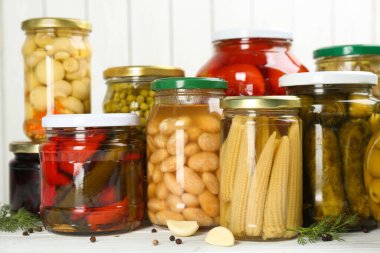 Beyaz ahşap arka planda farklı sebze turşusu ve mantar dolu cam kavanozlar.