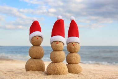Kumsalda kumdan yapılmış kardan adamlar ve deniz kenarında Noel Baba şapkaları. Noel tatili