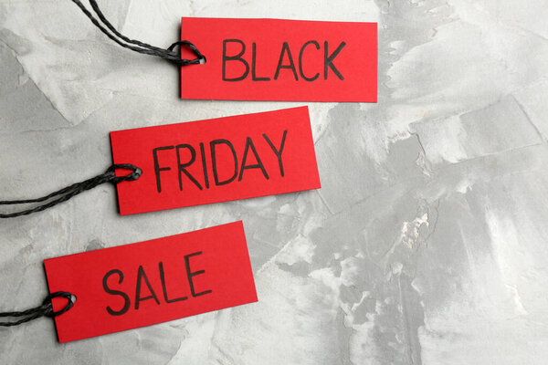 Red tags with words BLACK FRIDAY SALE on light grey stone background, flat lay. Space for text