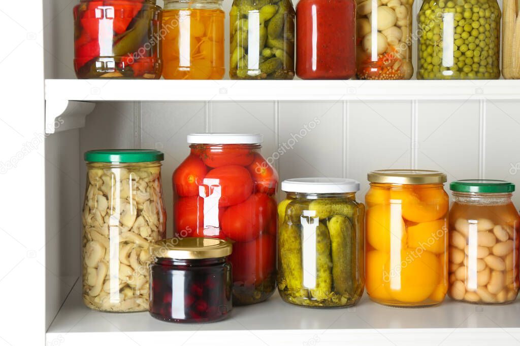 Jars of pickled fruits and vegetables on white wooden shelves