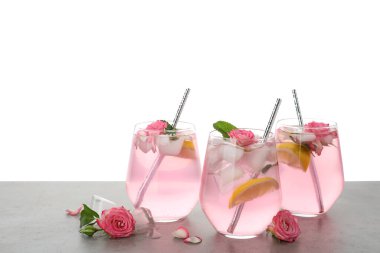 Gül çiçekleri ve açık gri masada beyaz arka planda limon dilimleri ile nefis ferahlatıcı bir içecek.