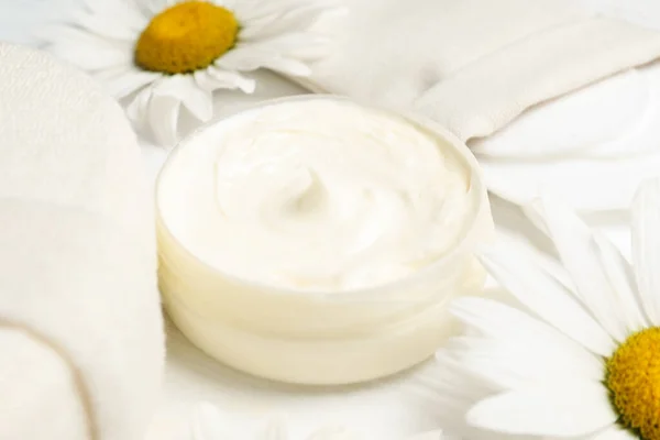 Composition with chamomile flowers and cosmetic product on white wooden table, closeup