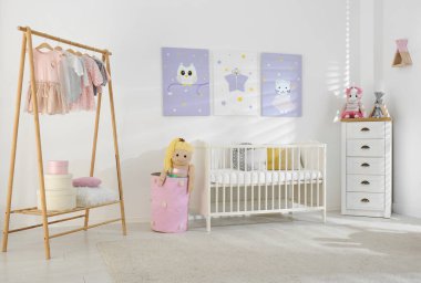 Bebek odasının içinde şirin posterler, karyola ve elbise rafları var.