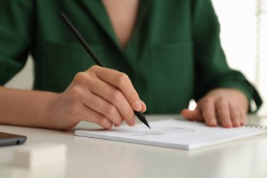 Beyaz masadaki kalemle çizen kadın, yakın plan.