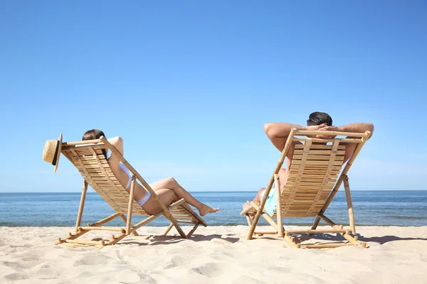 Woman in bikini and her boyfriend on deck chairs at beach. Lovely couple