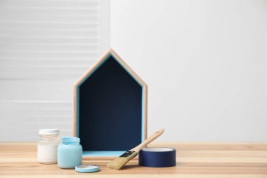 Ev şekilli raf, kavanozlar dolusu boya ve dekoratör aletleri masada. Metin için boşluk