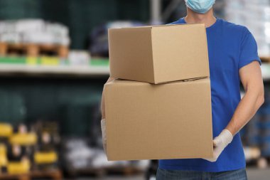 Üniformalı ve tıbbi maskeli bir adam. Dükkanda karton kutular var. Yakın plan. Toptan piyasa