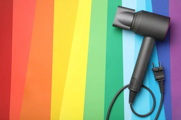Hair dryer on rainbow background, top view with space for text. Professional hairdresser tool