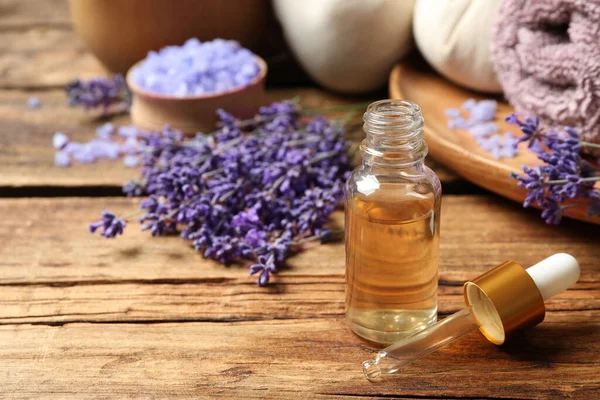 Composition with essential oil and lavender flowers on wooden table. Space for text