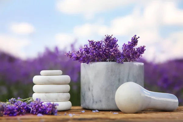 Spa stones, fresh lavender flowers and white marble mortar on wooden table outdoors, closeup