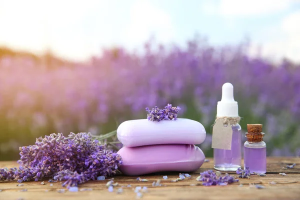 Fresh lavender flowers, soap bars and essential oil on wooden table outdoors, closeup