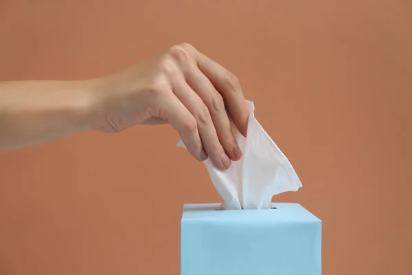 Woman taking paper tissue from box on light brown background, closeup