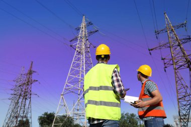 Yüksek voltaj kulelerinin yanında üniformalı profesyonel elektrikçiler.