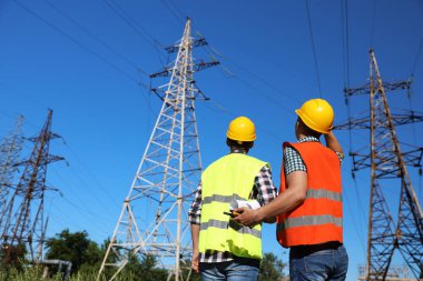 Yüksek voltaj kulelerinin yanında üniformalı profesyonel elektrikçiler.