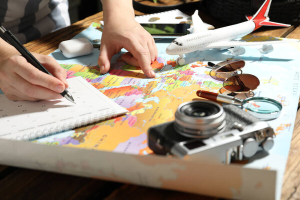 Woman marking calendar at table with world map, closeup. Travel during summer vacation