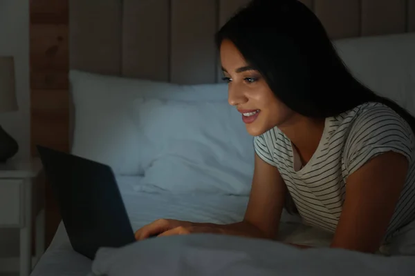 Happy woman using laptop in dark bedroom