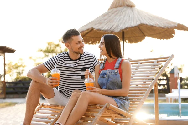 Happy couple with cups of refreshing drink resting in deck chairs outdoors