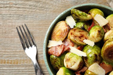 Lezzetli kızarmış Brüksel lahanası, kasede domuz pastırması, ahşap masa üzerinde çatal, düz uzanmış.