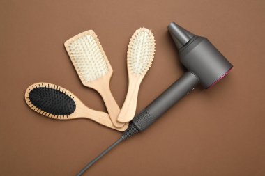 Saç kurutma makinesi ve kahverengi arka planda farklı fırçalar. Profesyonel kuaför aracı