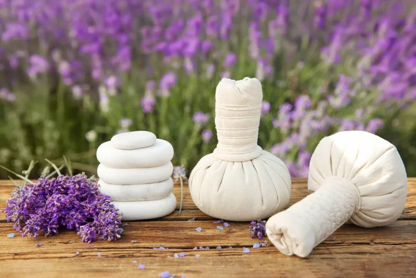 Spa stones, fresh lavender flowers and herbal bags on wooden table outdoors, closeup
