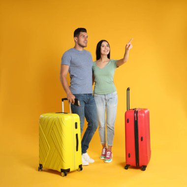 Sarı arka planda yaz gezisi için bavulları olan mutlu çift. Tatil gezisi
