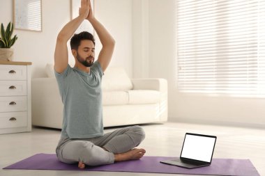Koronavirüs salgını sırasında evde online ders izlerken yoga yapan bir adam. Sosyal uzaklık