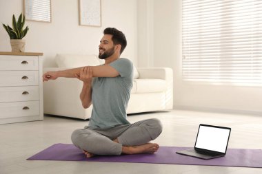 Koronavirüs salgını sırasında evde online ders izlerken yoga yapan bir adam. Sosyal uzaklık