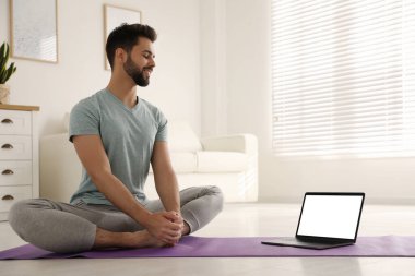 Koronavirüs salgını sırasında evde online ders izlerken yoga yapan bir adam. Sosyal uzaklık