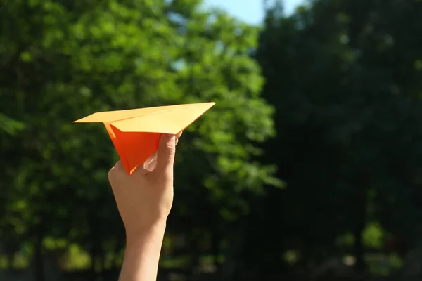 Woman holding paper plane outdoors, closeup. Space for text