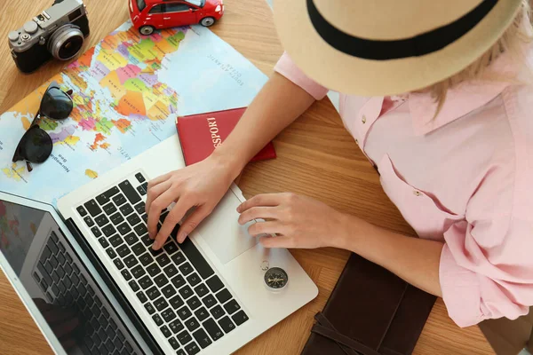 Woman using laptop to plan trip at wooden table, closeup