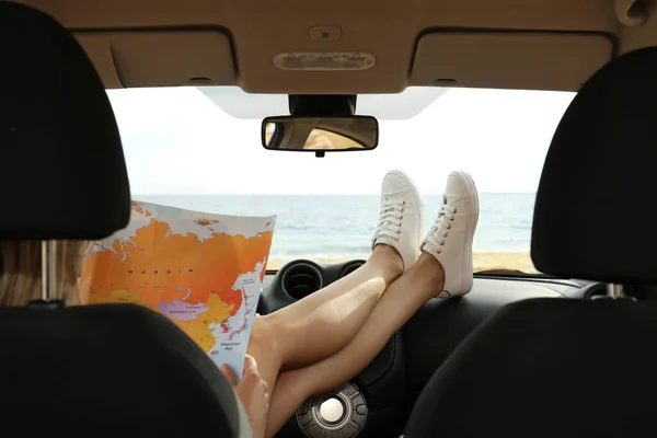 Young woman with world map in car, back view. Road trip