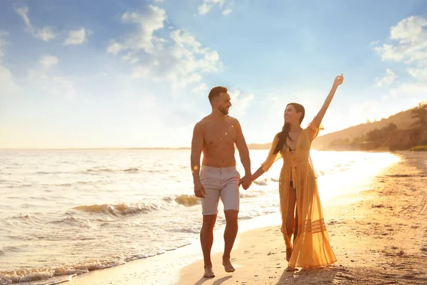 日落时一对快乐的年轻夫妇一起在海滩上散步 — 图库照片